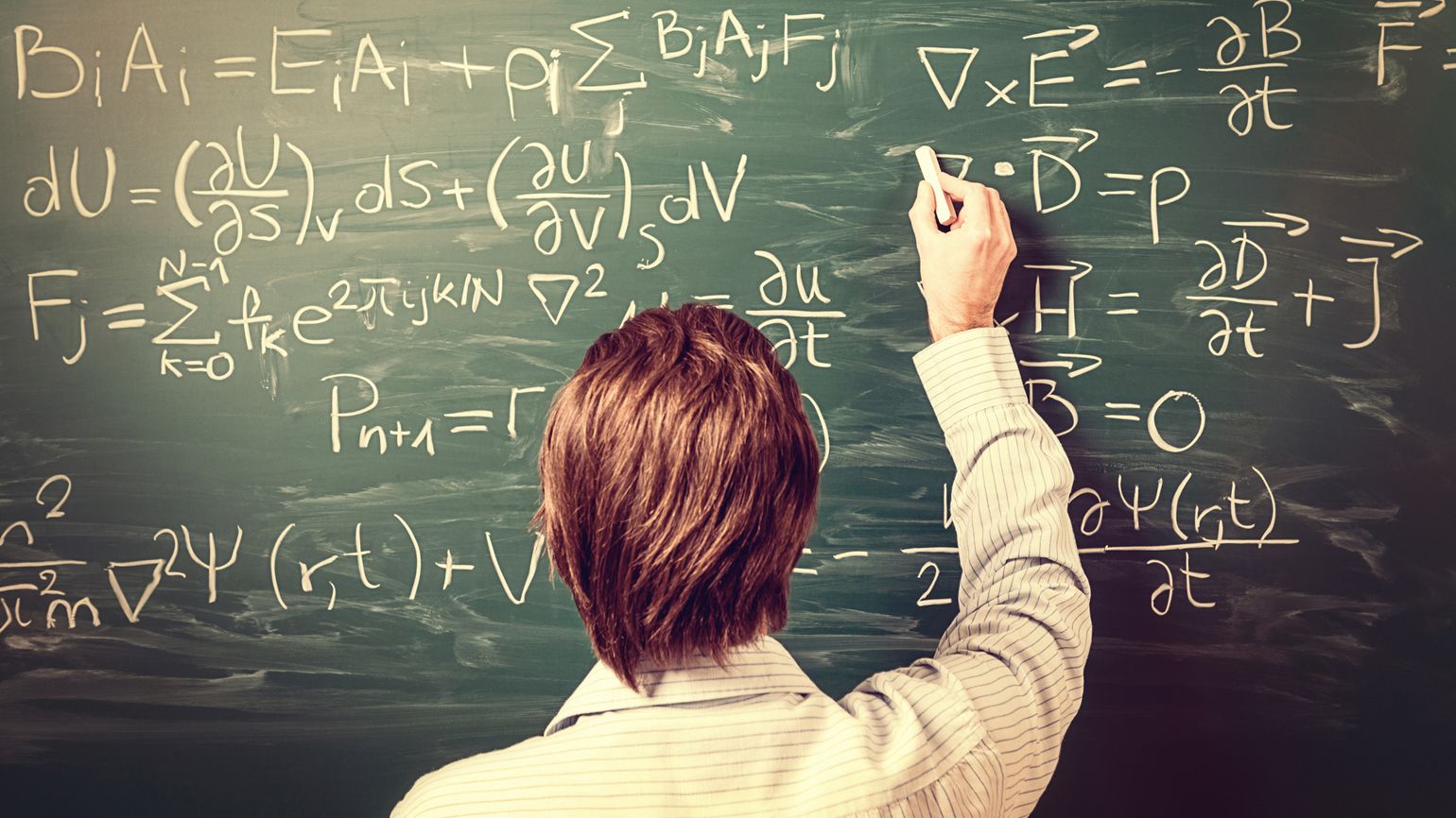 A man solves physics equations on a chalkboard.