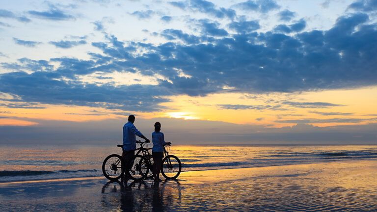 Couple riding their bikes on the beach at sunset