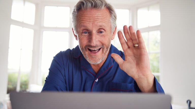 An older gentleman greeting someone on his laptop.