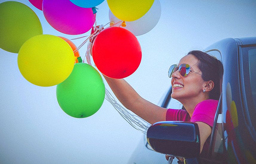Cheerful woman holding balloons out of a car window