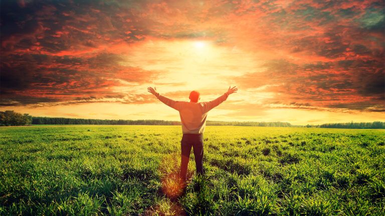 A man stands in a field, welcoming the sunrise