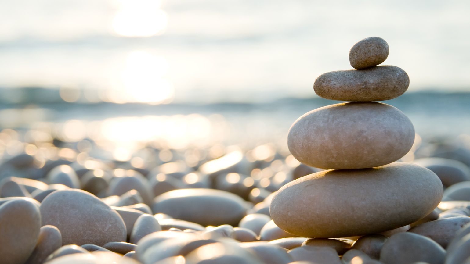 Balanced stones on a pebble beach during sunset.