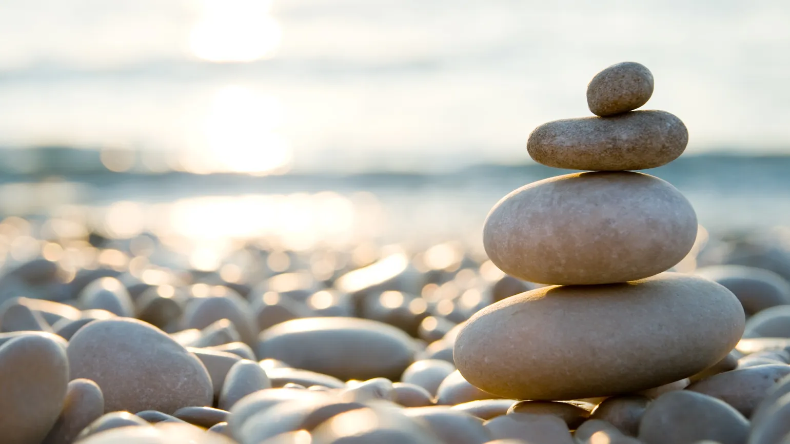 Balanced stones on a pebble beach during sunset.