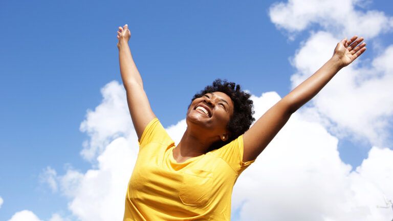 A smiling woman holds her arms aloft in joy