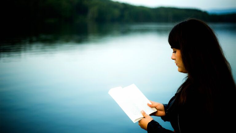 A woman reads a Bigle by a lake