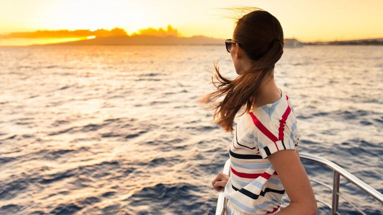 A woman stands at the bow of a ferry, gazing out at the sunrise