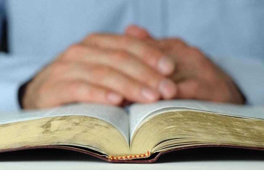 Man's praying hands over bible