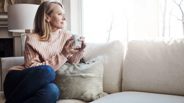 A woman gazing out a window with a cup in her hand.