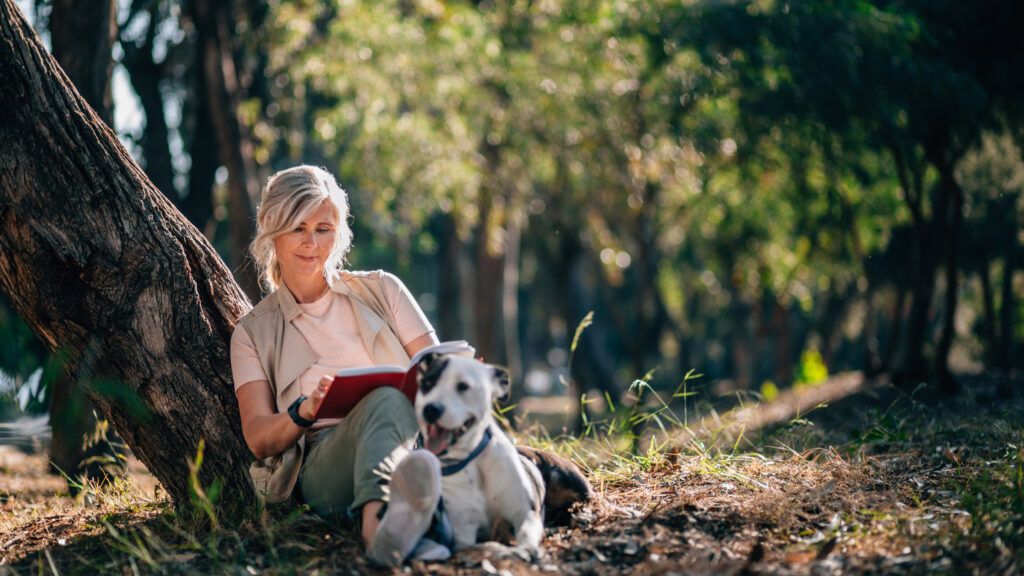A woman reading outside with her dog.