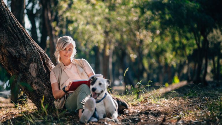 A woman reading outside with her dog.