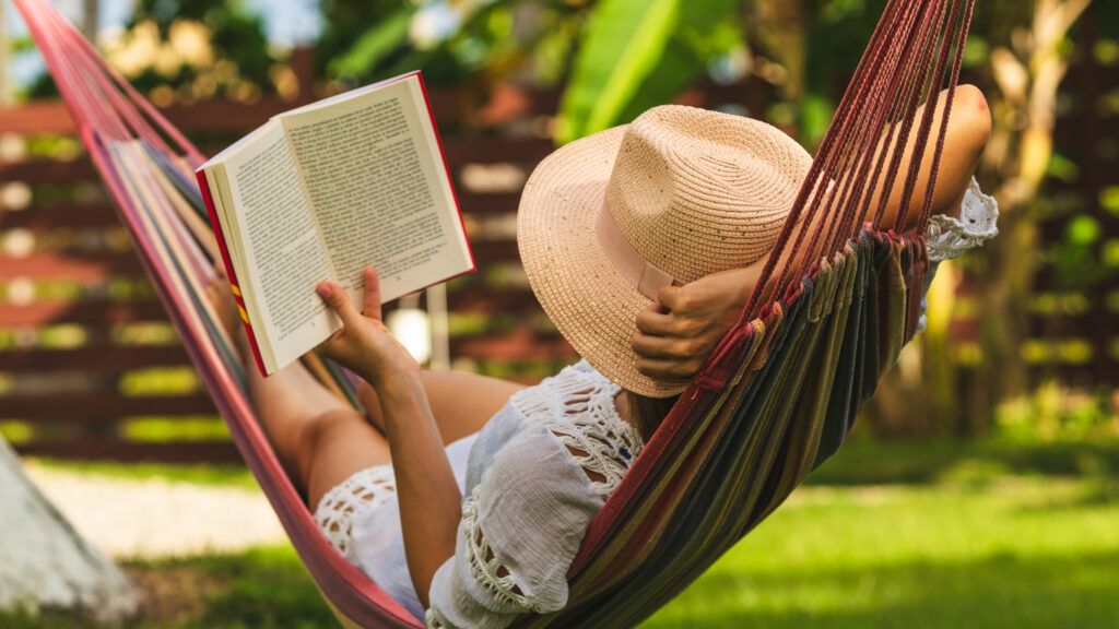 A woman reading a book in a hammock.