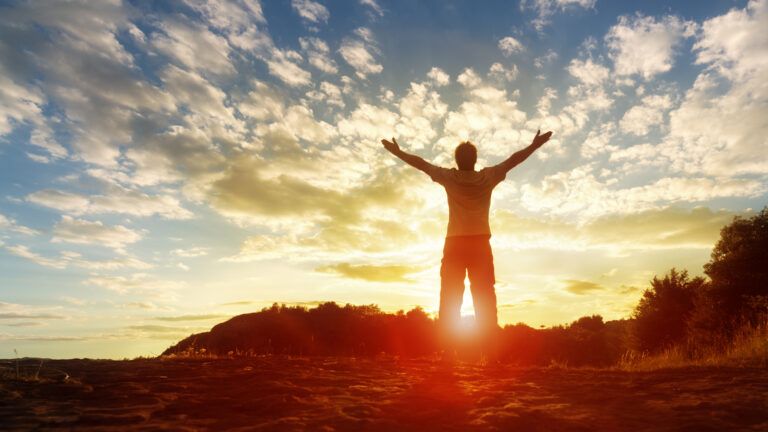 Man facing the sunrise with open arms