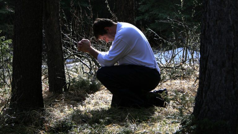 A man kneels in prayer in the woods