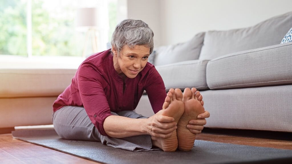 An older woman stretching in her home.