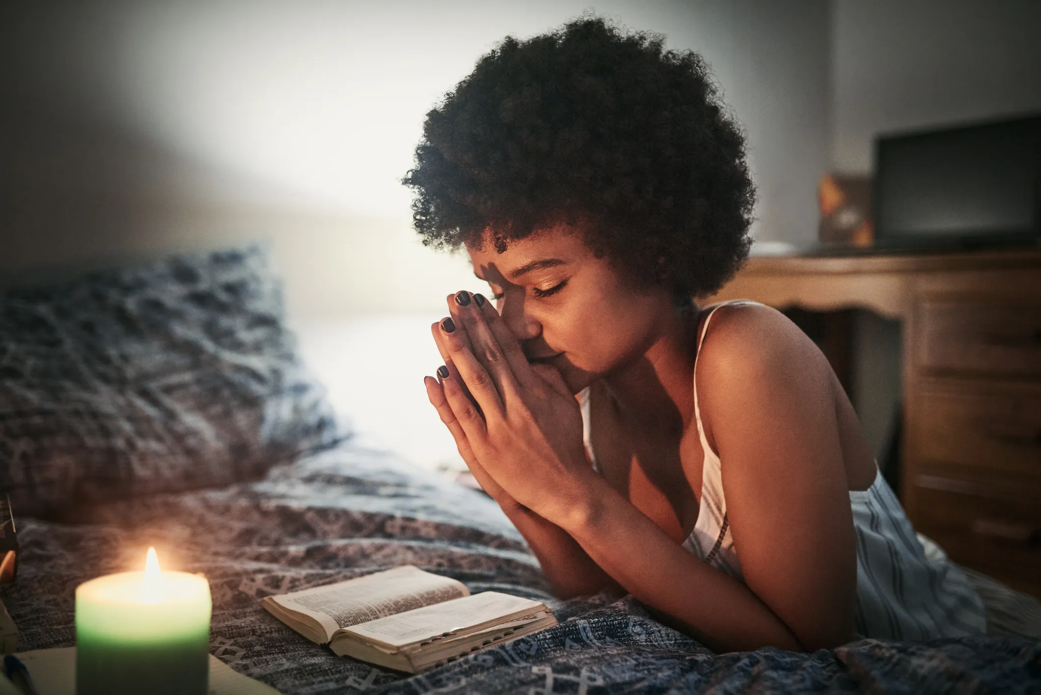 A woman praying by her bedside.