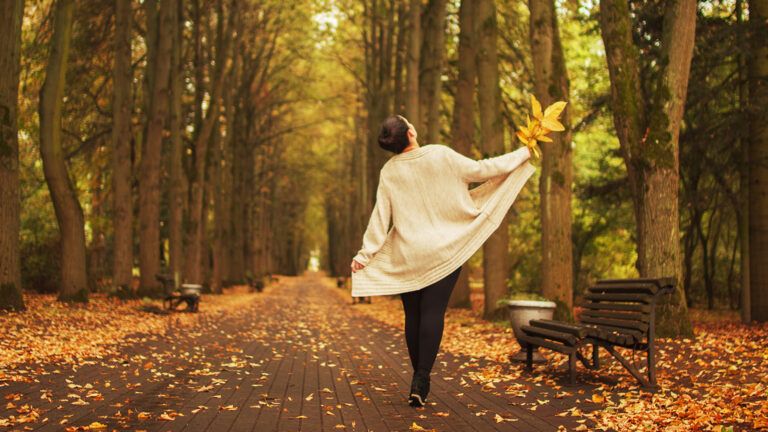 A woman takes a joyful stroll through a park in autumn
