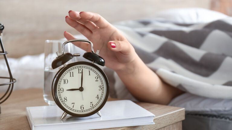 A woman reaching for her alarm clock; Getty Images
