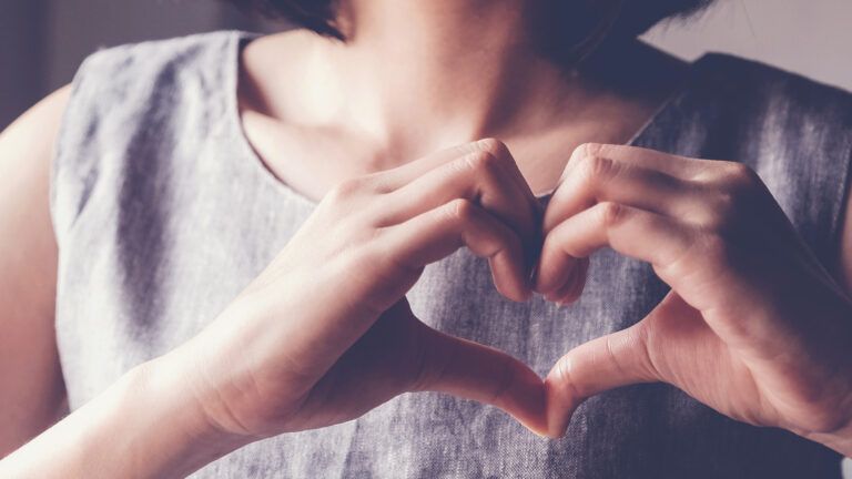 A woman making a heart with her hands; Shutterstock