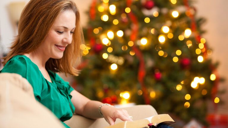 A woman reads her Bible by a Christmas tree