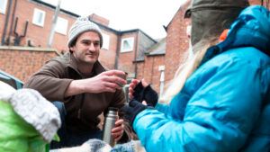 A man gives hot soup to a homeless person