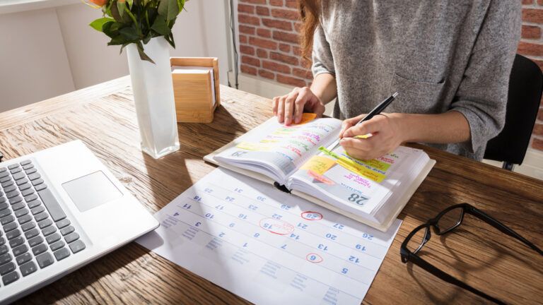 A woman organizing her day using an annual paper planner; Getty Images