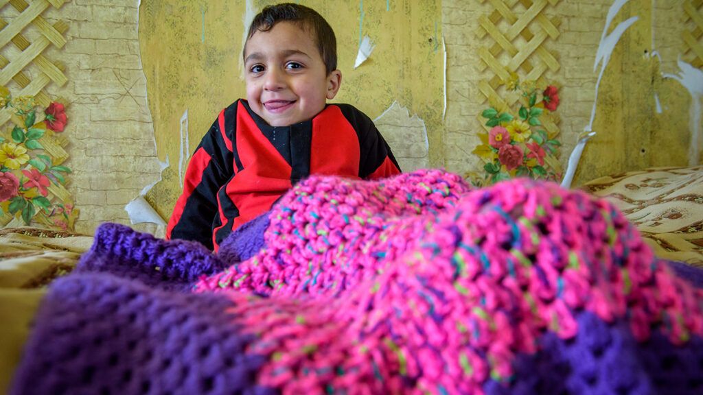 Four-year-old Serghik Mikayelyan sits under a Knit for Kids blanket