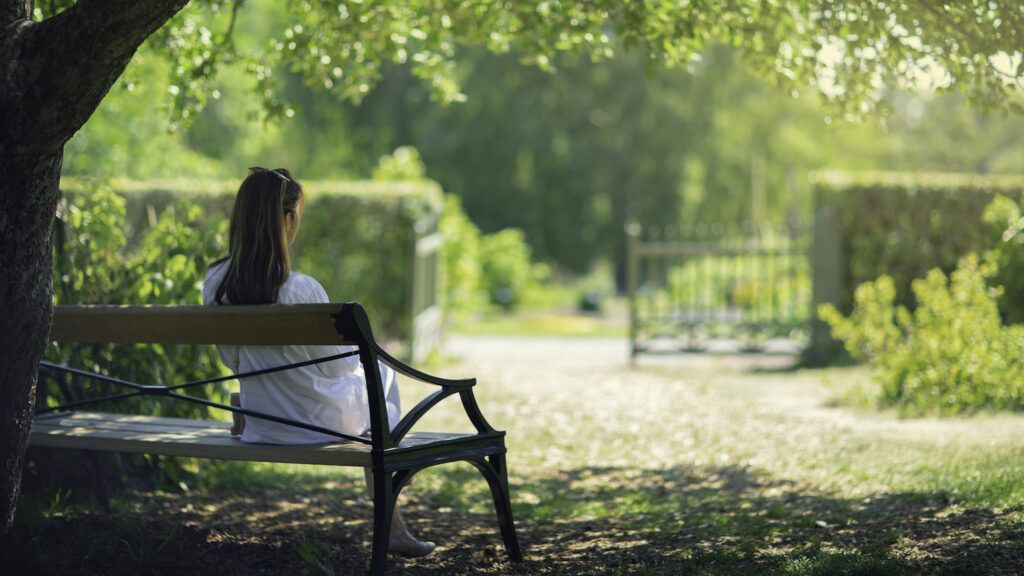 A woman sitting on a bench at the park learning how to do lent in a new way