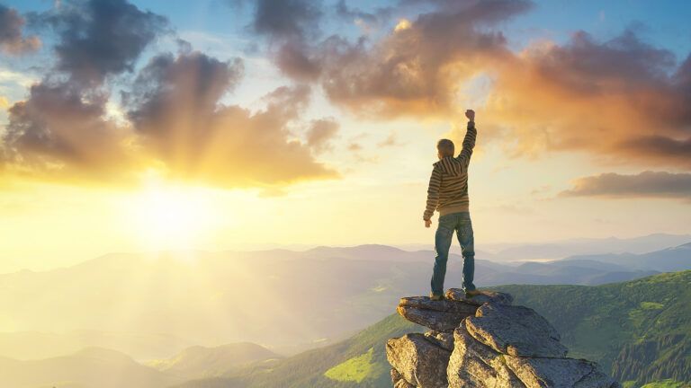 A triumphant man greets the sunrise from atop a cliff