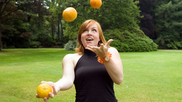 A young woman juggles three oranges