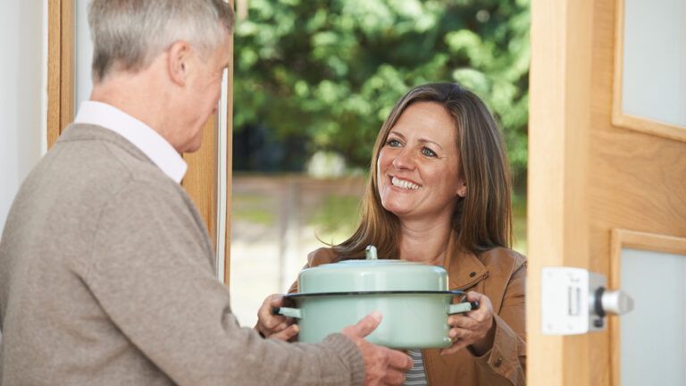 A woman brings a casserole to a neighbor