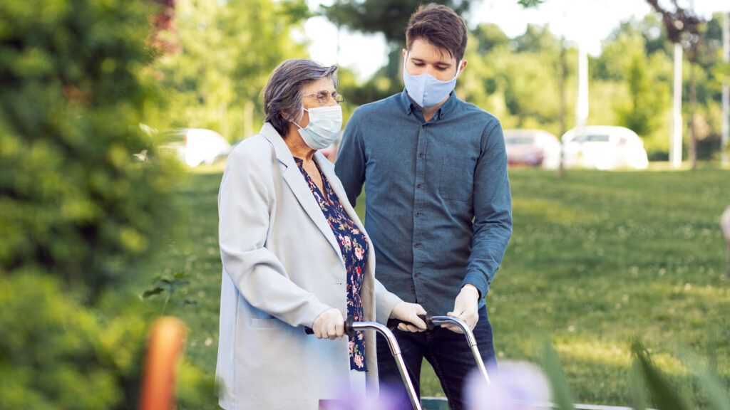A young man helping an older woman wearing protective face masks; Getty Images