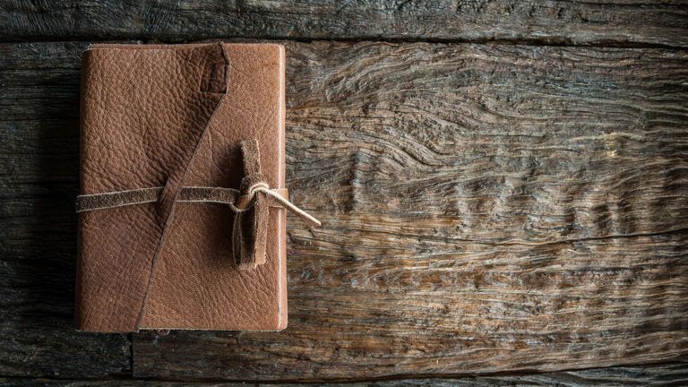 A leather-bound journal rest on a rustic wooden table; Getty Images