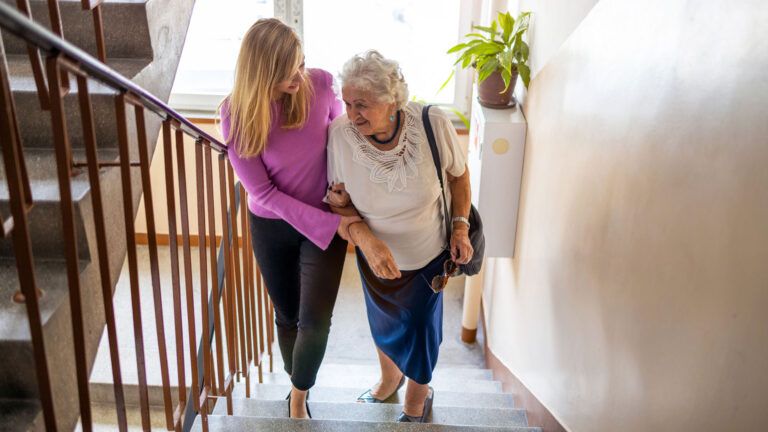 A woman helping an elderly woman up the staircase; Getty Images