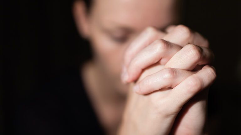 A woman clasps her hand in prayer