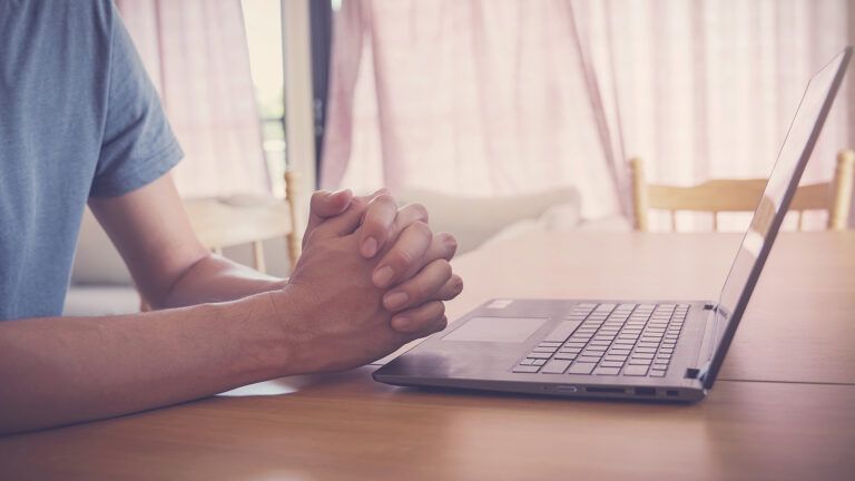 Praying hands near a laptop