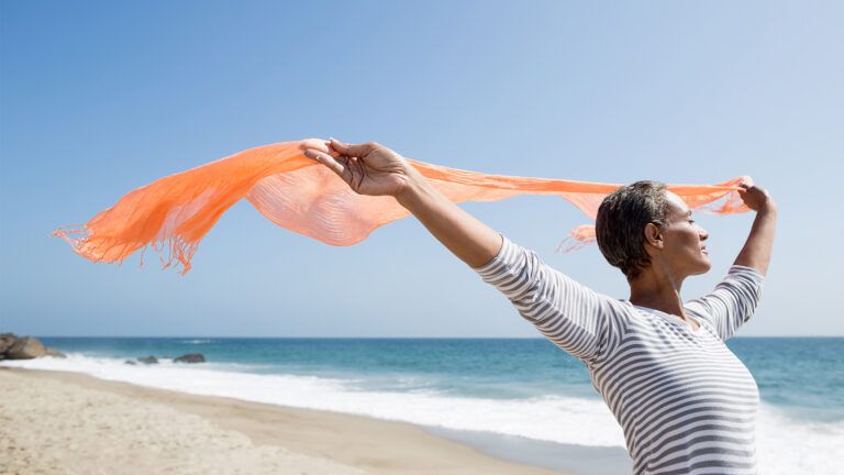 A woman on a beach lets sea breezes blow through her scarf