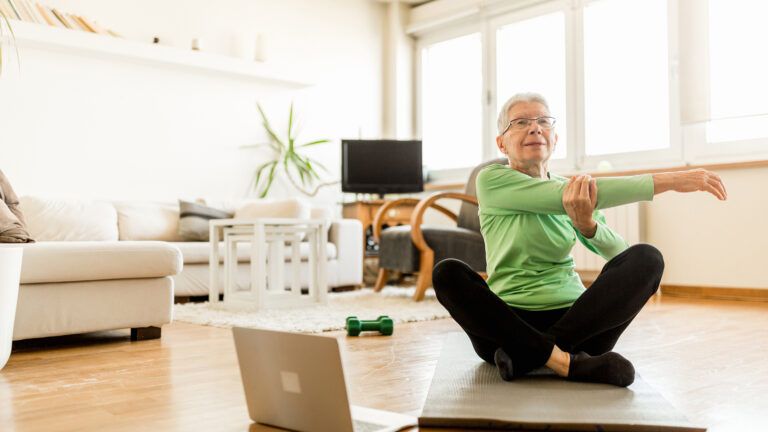An aging woman stretching indoors; Getty Images