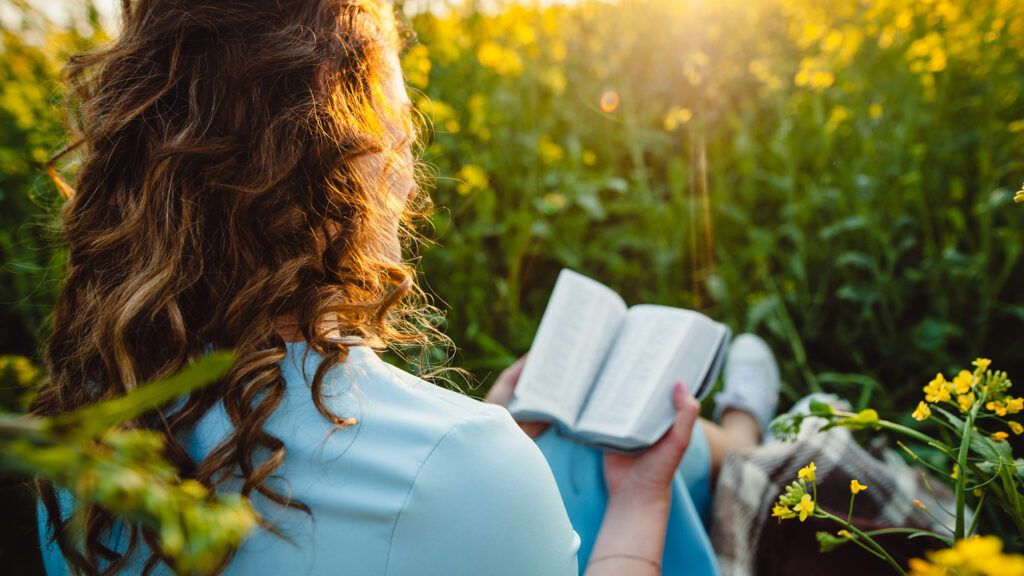 A woman reading the Bible in the grass; Getty Images