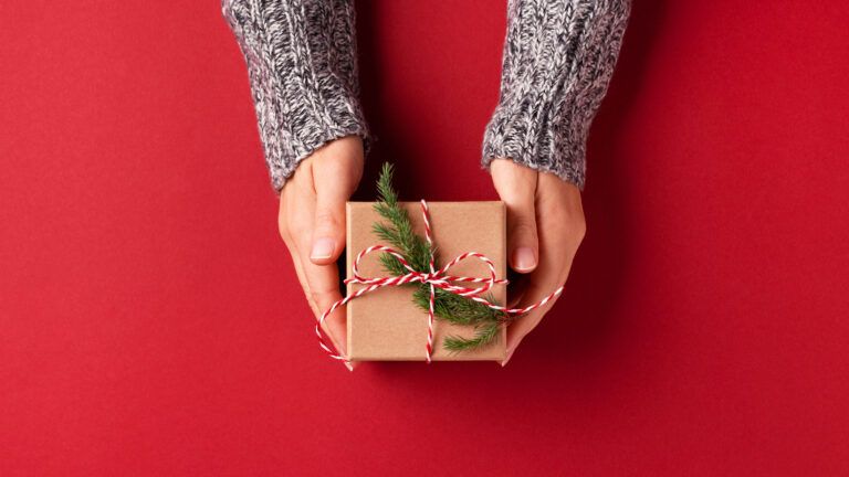 Hands holding a faith gift for Christmas 2022 on a red background