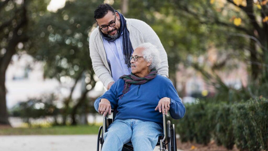 A senior man in a wheelchair conversing with his caregiver; Getty Images