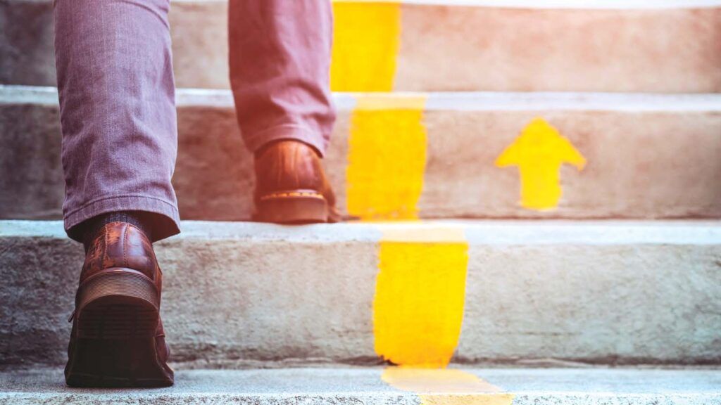 A man walking up stairs with yellow up arrows; Shutterstock