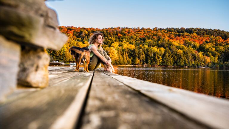 A woman sits on a lakeside pier in autumn