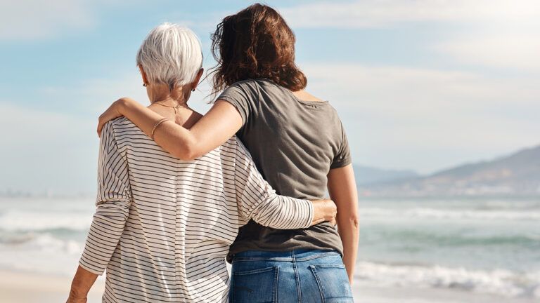 An adult woman and her senior mother walk along a beach