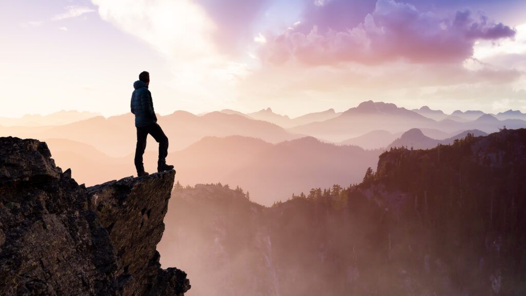 Man standing on a cliff thinking about God's hands