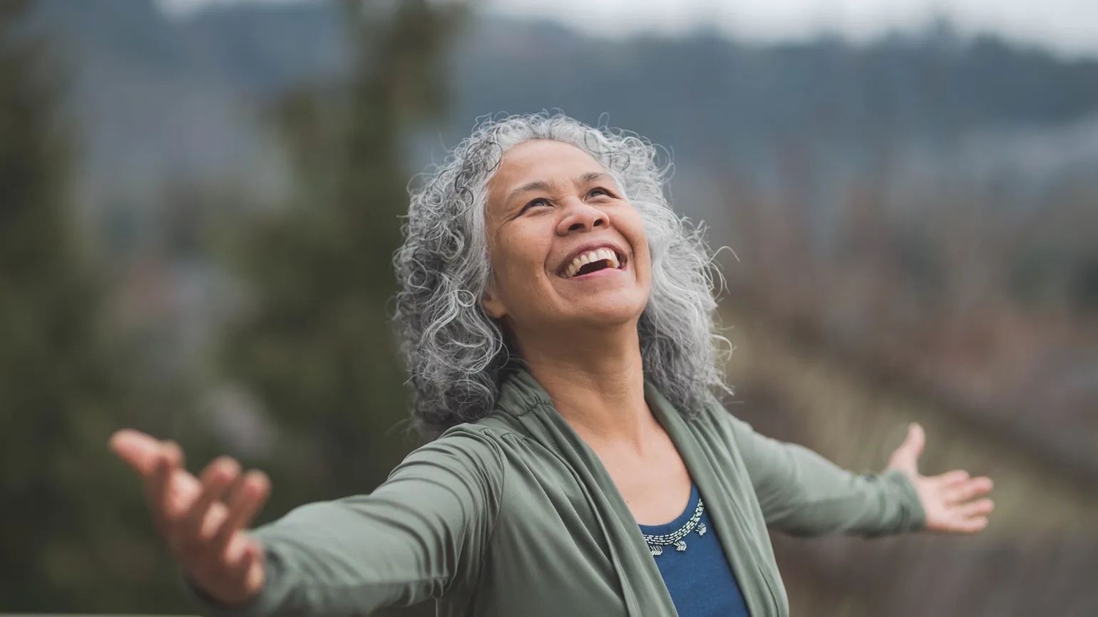 A woman outside with her arms outstretched giving thanks to God's hands