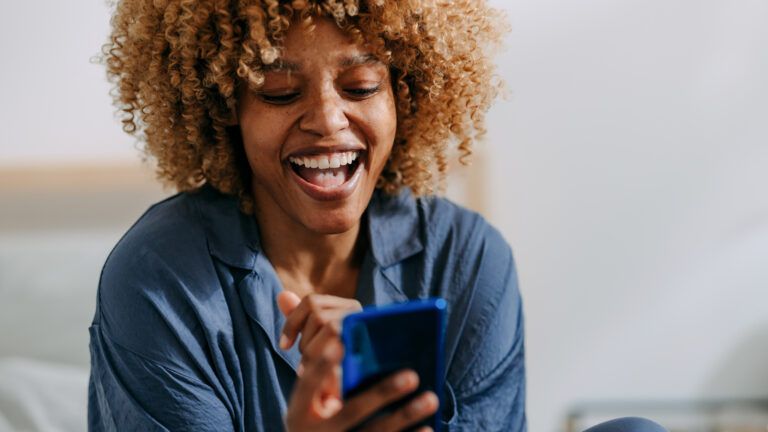 Woman laughing at something funny on her phone to avoid doomscrolling