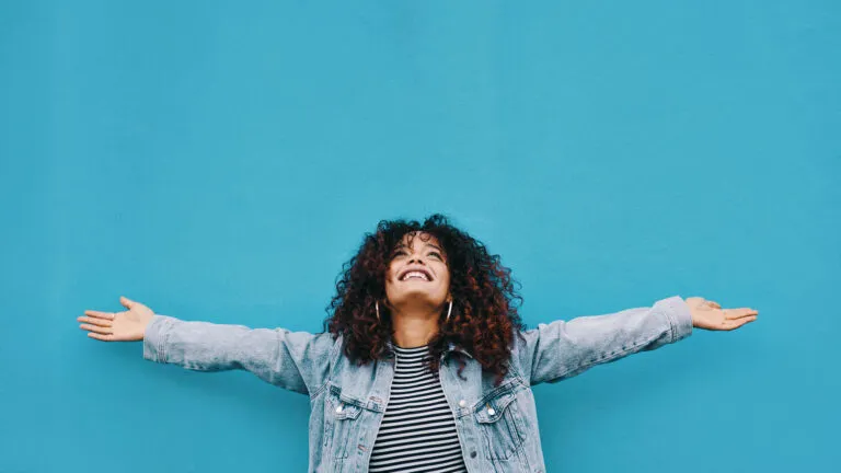 Woman with her arms up in front of a blue wall after reading Easter Bible verses