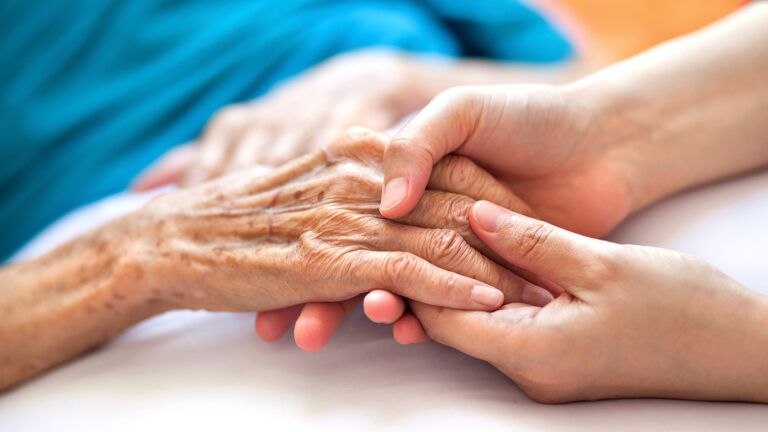 Caregiver's hand holding senior's hand