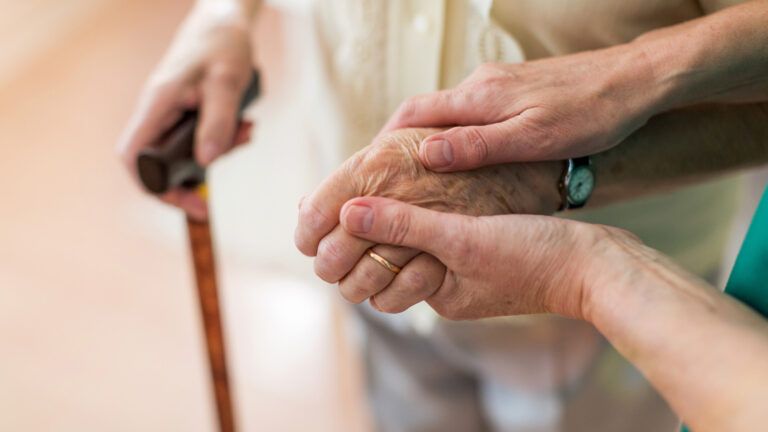 Caregiver holding the hands of an aging woman; Getty Images