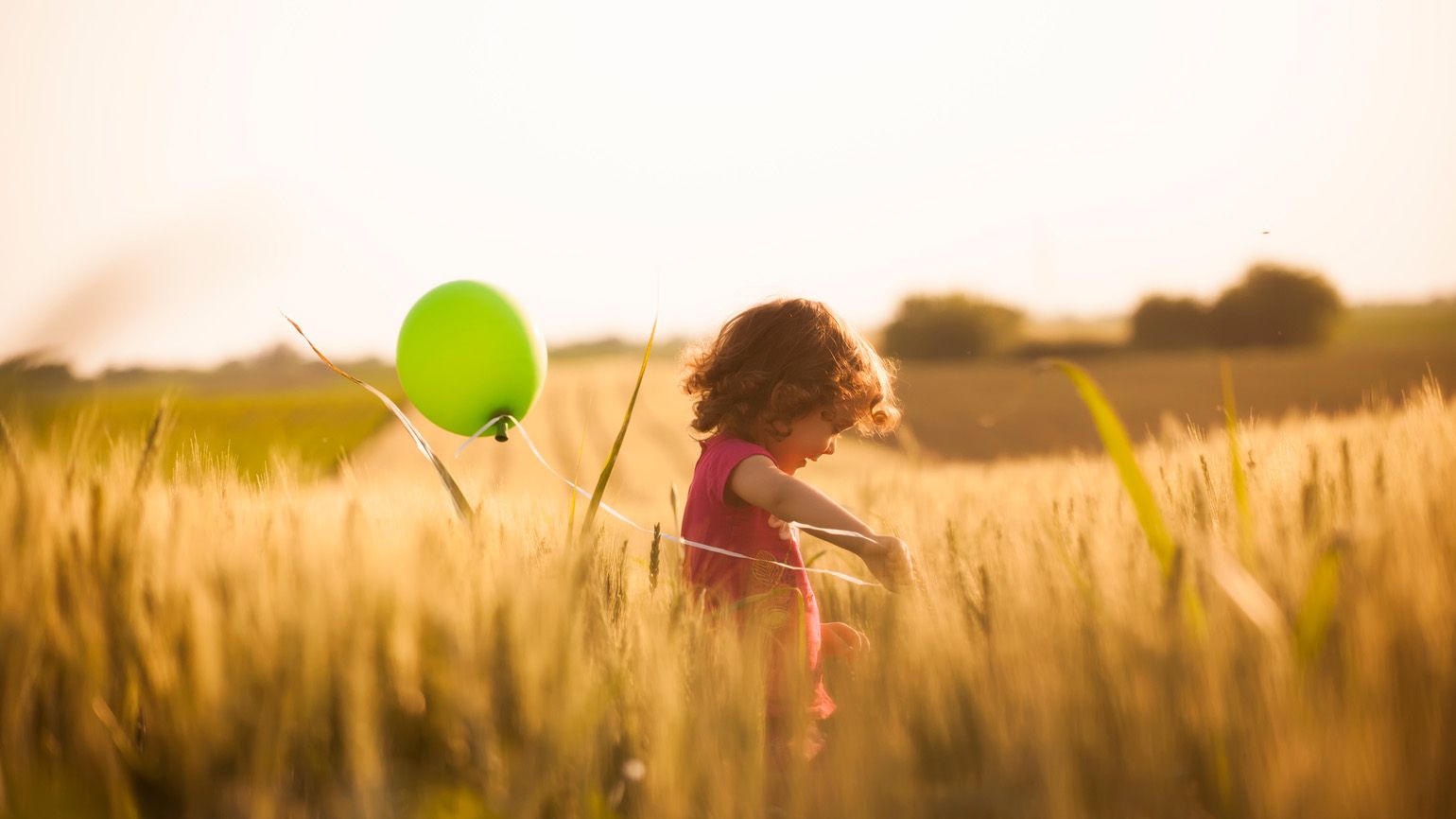 Young child frolicking in a field with a green balloon; Getty Images